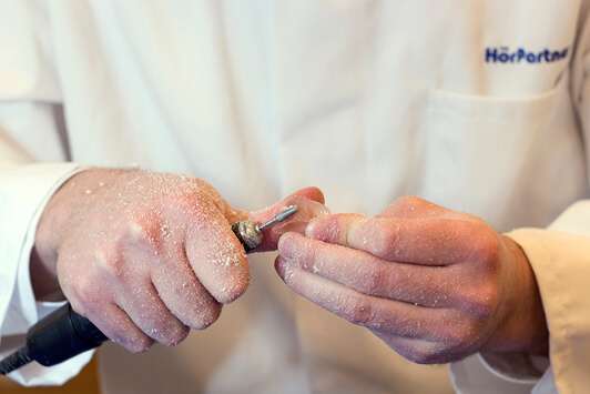 Ein Hörakustiker bearbeitet ein Hörgerät mit einem Fräswerkzeug in der Hand.